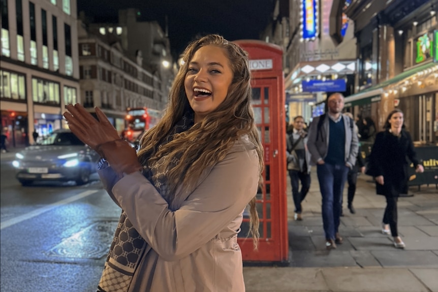 Naarah poses sidewards to camera, smiling, with her hands up together wearing gloves in London 