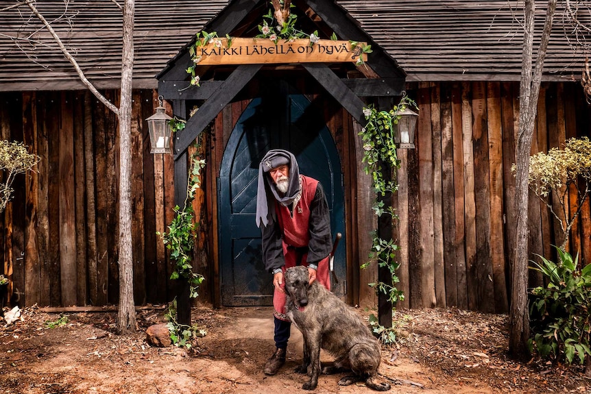 A man and large wolfhound dog outside a timber hut type building dressed in medieval clothing.