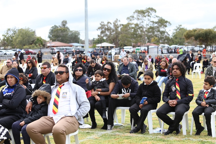 Mourners, wearing the Indigenous colours of black, red and yellow attending an outdoors funeral