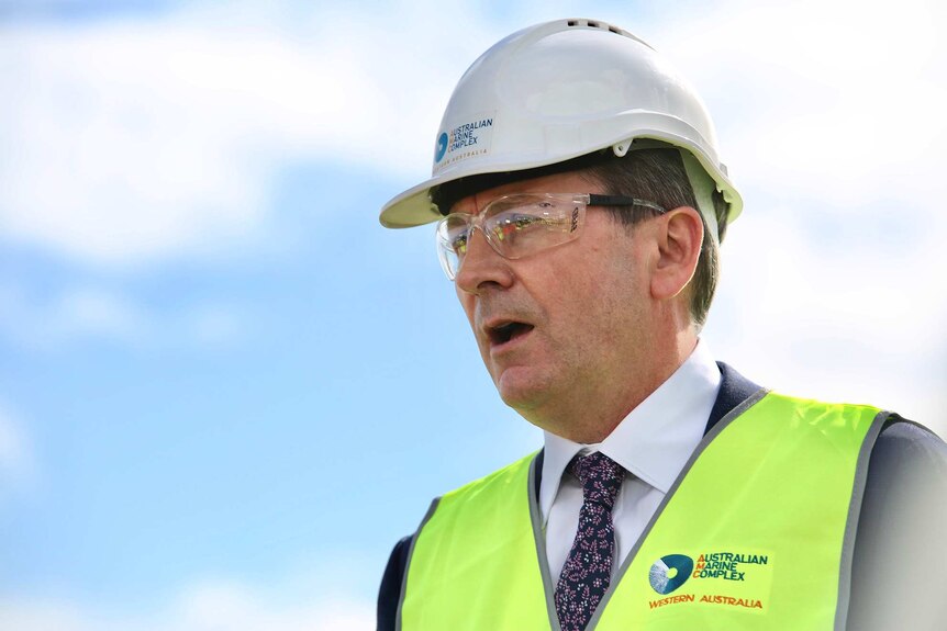 A head and shoulders shot of Mark McGowan wearing a hard hat, safety glasses and hi-vis vest with blue sky and clouds behind.