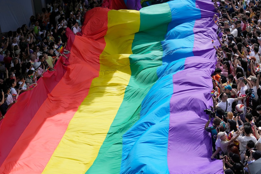 A rainbow flag is held up by hundreds of people at a pride street parade
