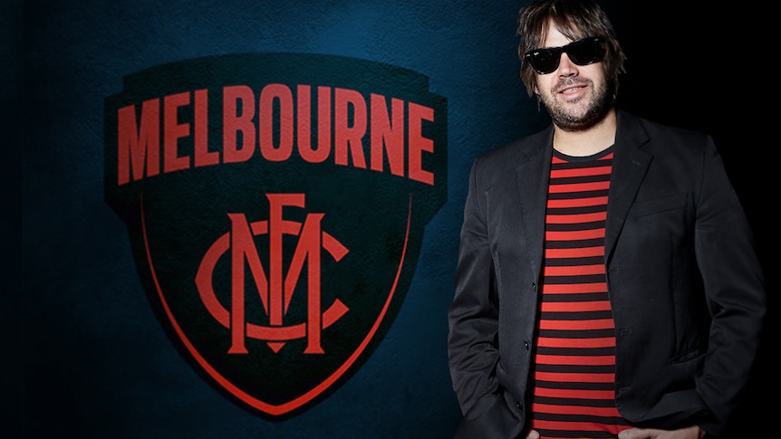 A red and blue logo reads Melbourne, with interlocked letters MFC. Unshaven man in sunglasses and striped t-shirt.
