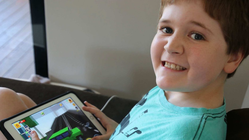 Joseph Dainton plays on his iPad and smiles for the camera.