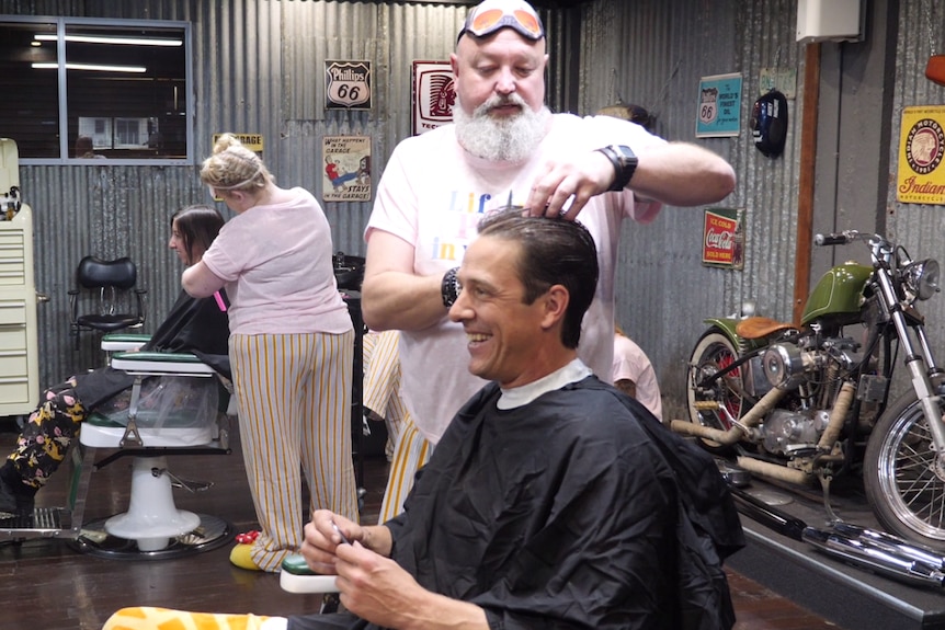 Samuel Johnson sits smiling in the barber's chair while Rex Silver gives him a trim.