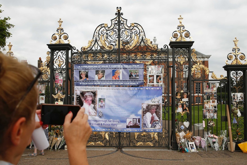 A tourist takes a smartphone photo of tributes and memorabilia for the late Diana, Princess of Wales outside Kensington Palace.