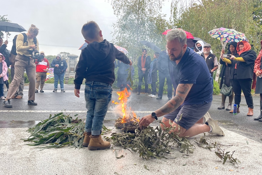 A man and boy standing near a pile of leaves on fire