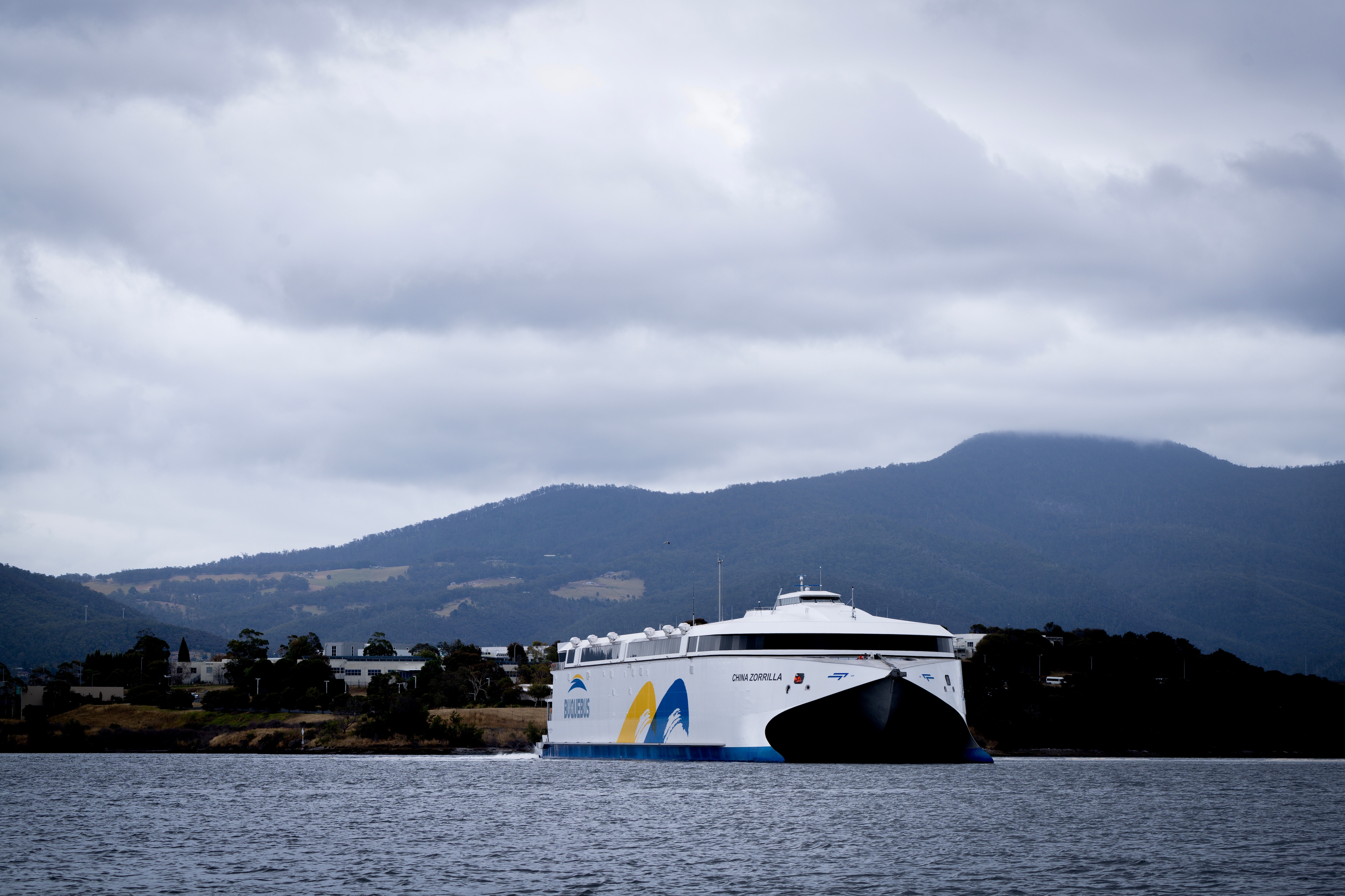 Un gran barco blanco en un río en Hobart con montañas al fondo. 