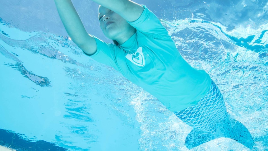 A young girl swims with a mermaid tail.