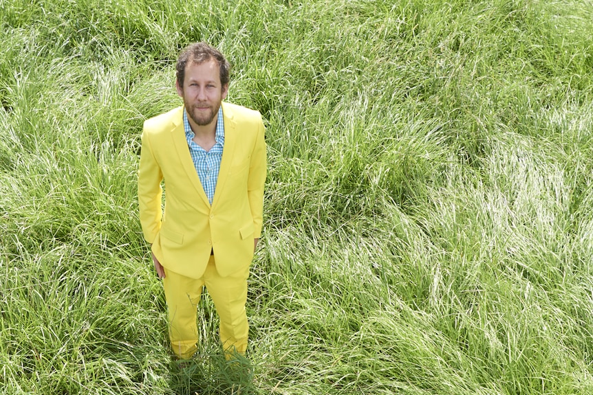 Australian musician, Ben Lee, stands in long, green grass.