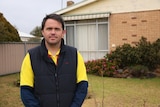 A man stands in front of a brick rental property.