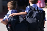 two young school boys walk to school wearing backpacks as one puts his arm around the others shoulder