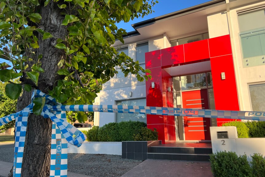 Blue and white police cordon tape in front of a house with a red door. 