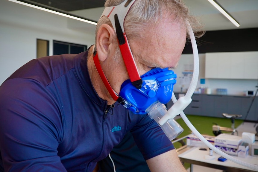 A man on a stationary bike, with an oxygen mask over his mouth, completing training