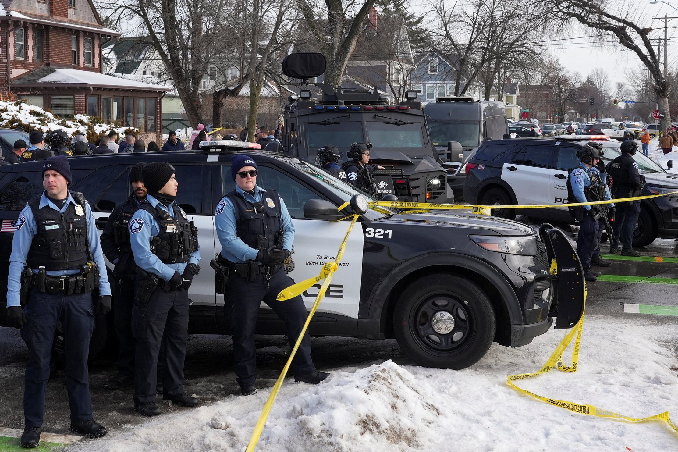 La policía y los vehículos policiales detrás de la cinta policial con una multitud de personas al fondo.