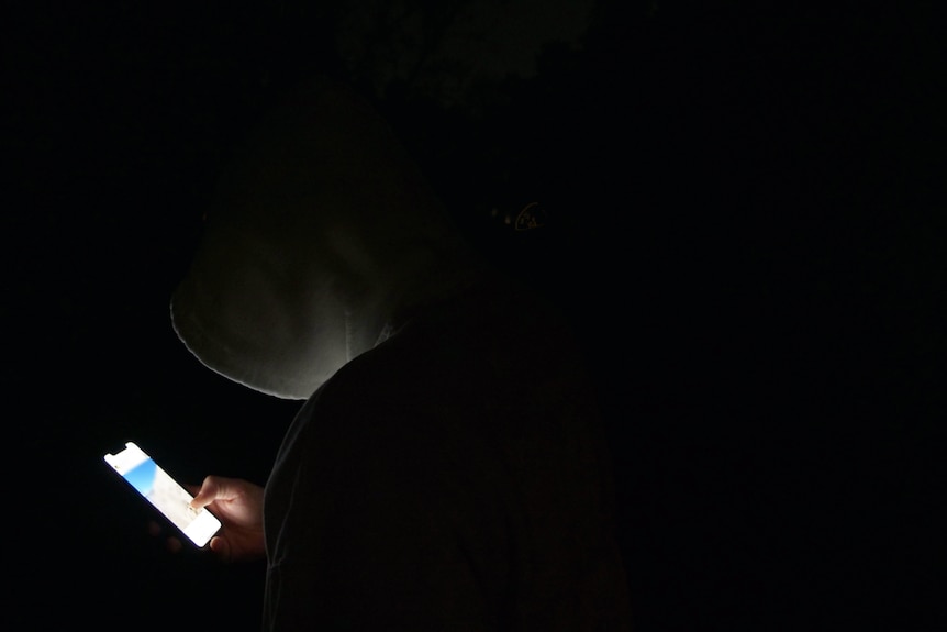 Hooded person at night looking at their phone