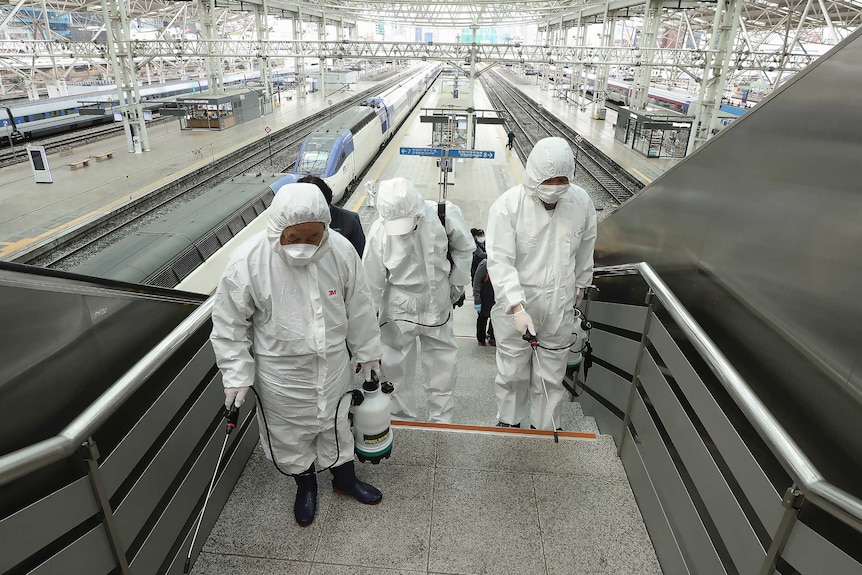 Three men in white protective suits and face masks spray downwards as they walk up stars.