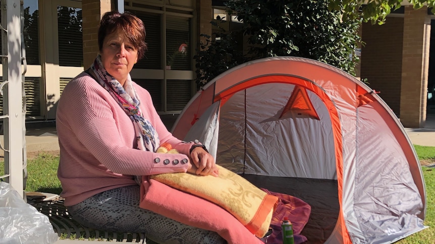 A woman sits in front of a tent, holding some blankets