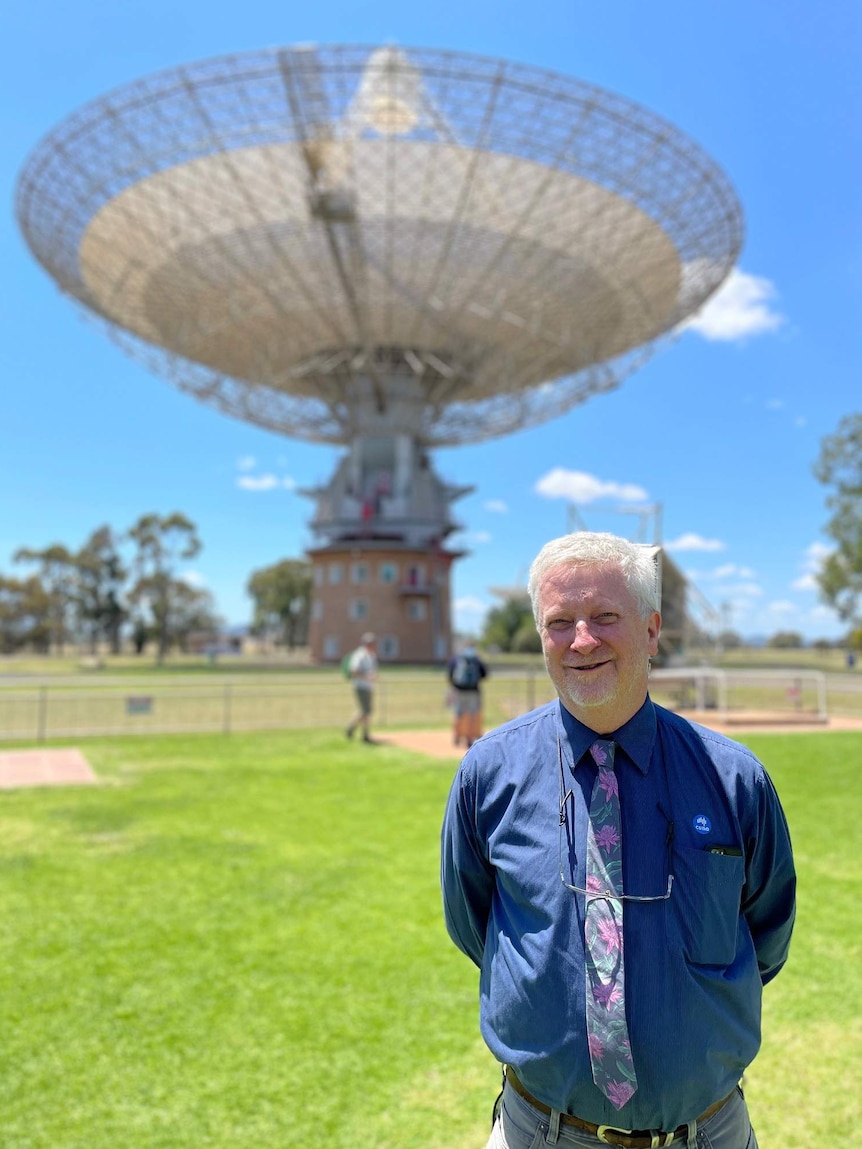 A man stands in front of the Parkes radio telescope.