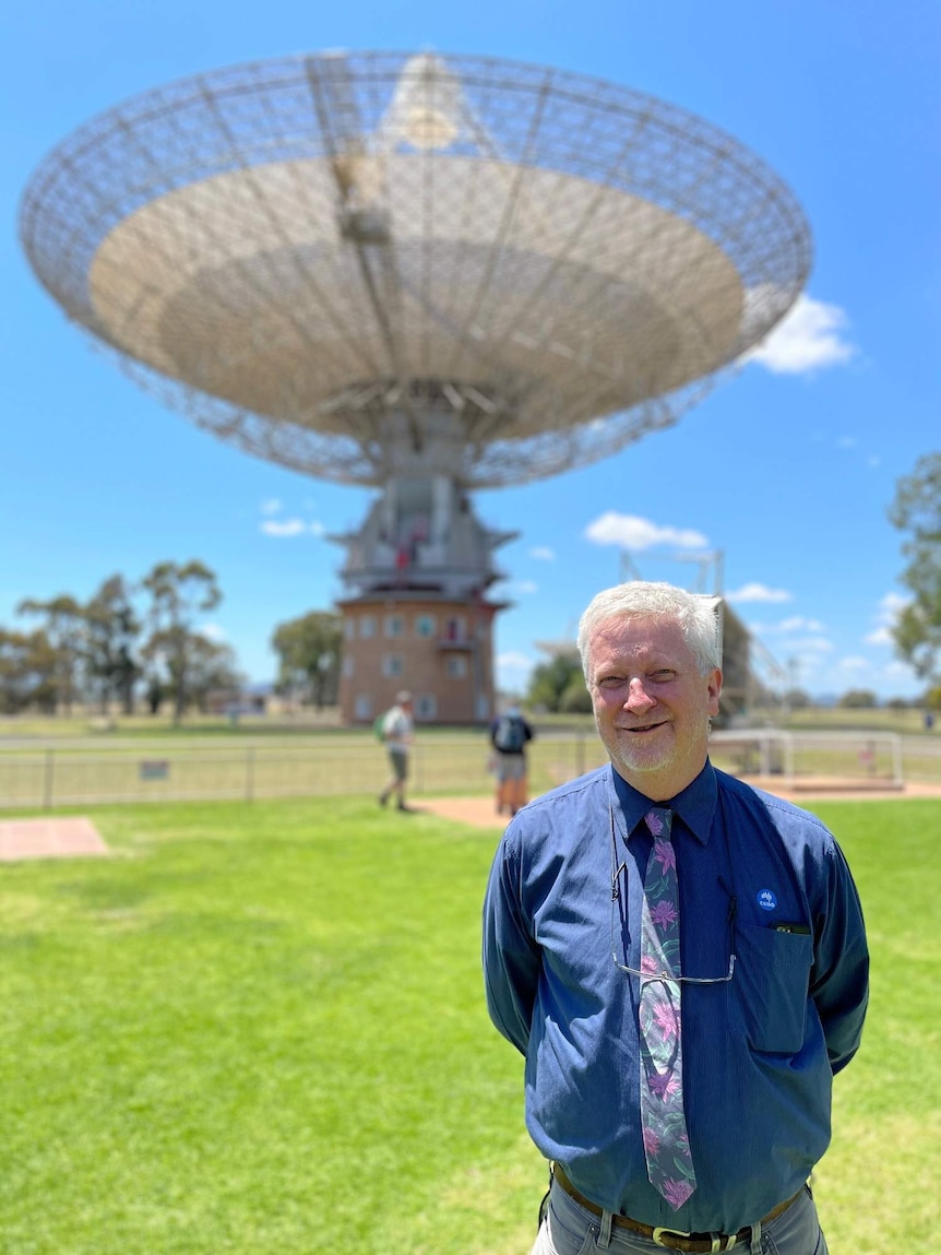 A man stands in front of the Parkes radio telescope.