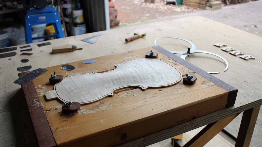 The back section of a violin sits on a workshop bench.