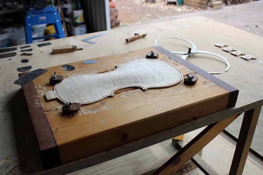 The back section of a violin sits on a workshop bench.