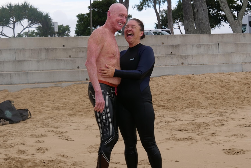 Two people in wetsuits smiling after a swim at the beach