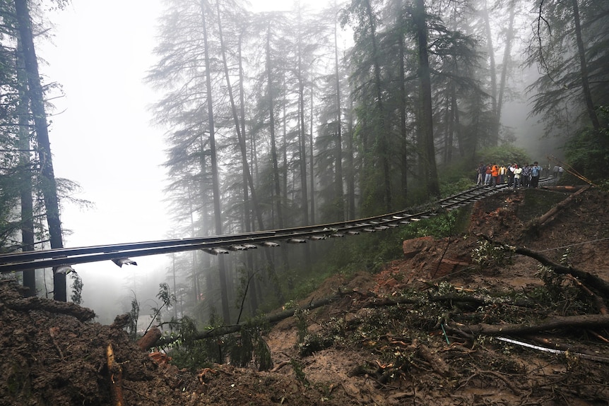 A railway track hangs over the edge of a landslide in a forest