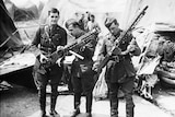 Soldiers of the WW1 allied forces holding guns in front of a plane wreckage.