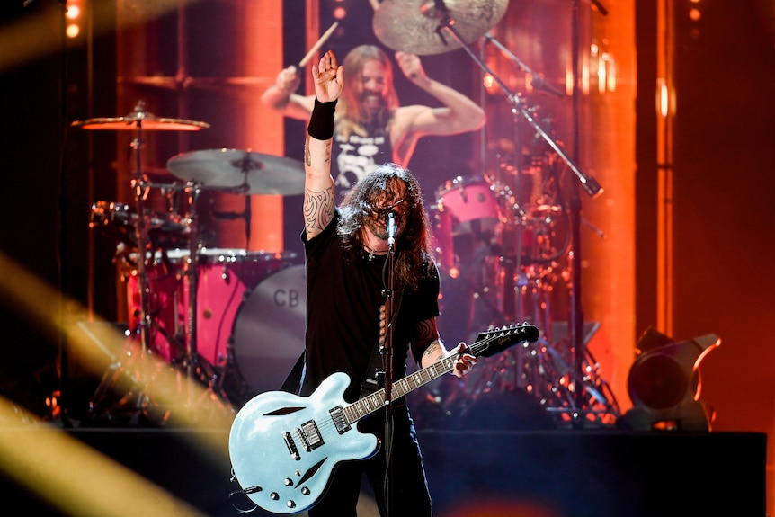 Dave Grohl sings into a microphone with Taylor Hawkins playing drums behind him