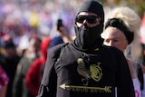 Man wearing balaclava and dark sunglasses, dark shirt in crowd