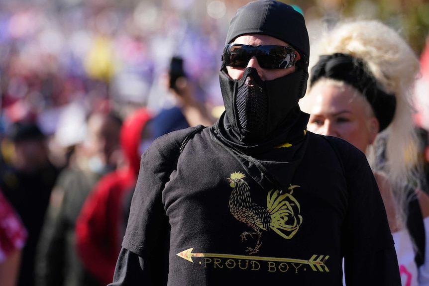 Man wearing balaclava and dark sunglasses, dark shirt in crowd