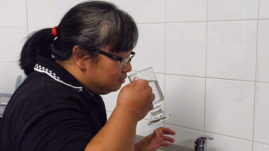 A woman takes a drink of water from a glass.