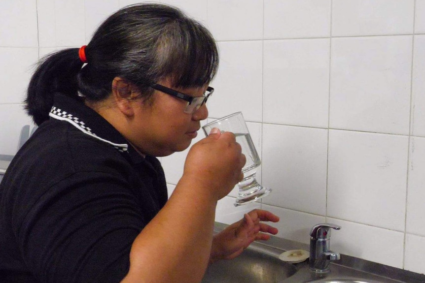 A woman takes a drink of water from a glass.