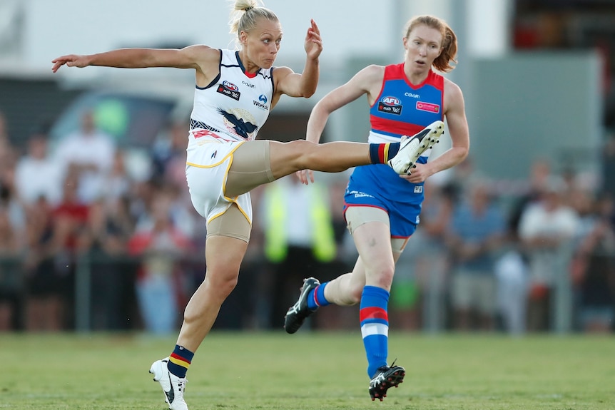 The muscles in Erin Phillips' leg flex as the AFLW star kicks the ball downfield for the Crows as a Bulldogs player looks on. 
