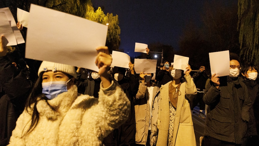 A group of people in masks holding a blank white paper. 