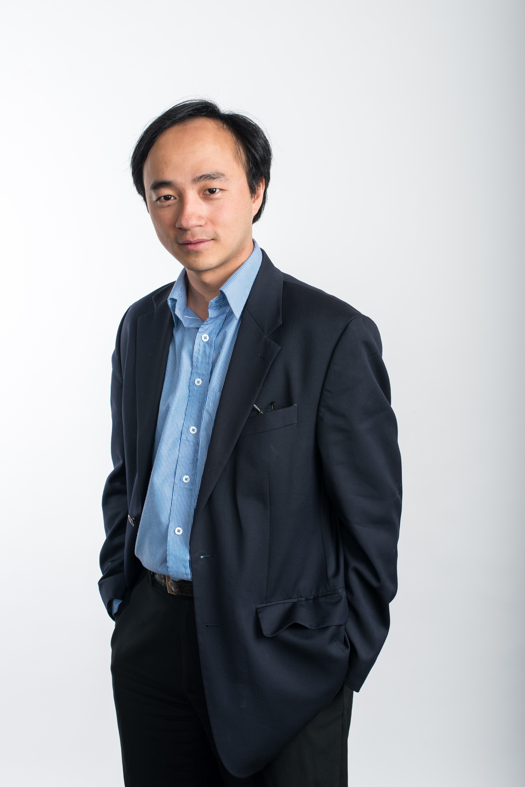 Professor He Yang Hui stands against a white background with his hands in his pockets.