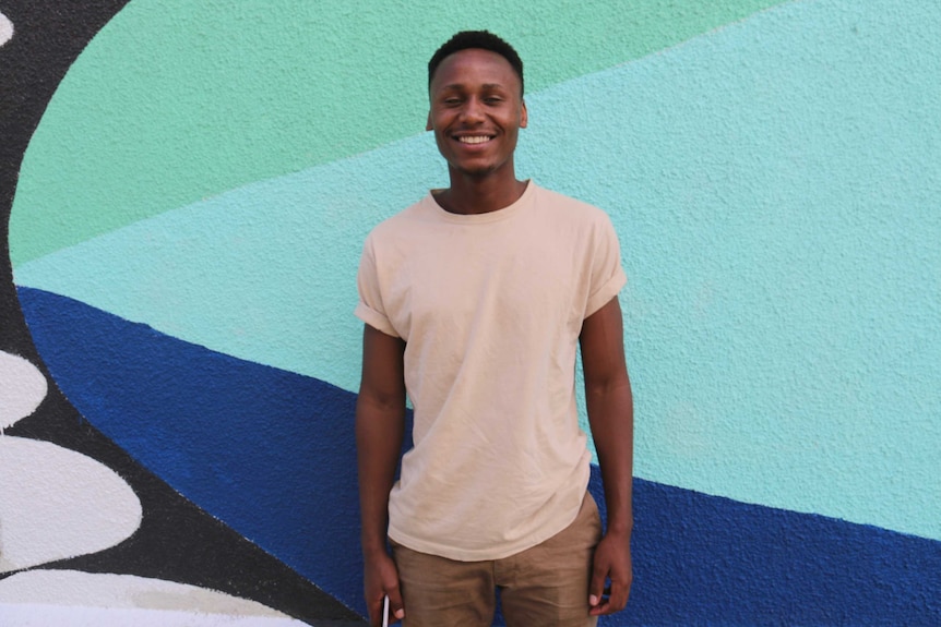 A young man stands in front of a wall.