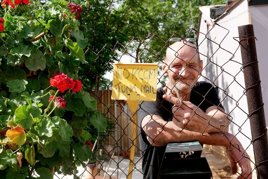 A man standing near a fence at his house.
