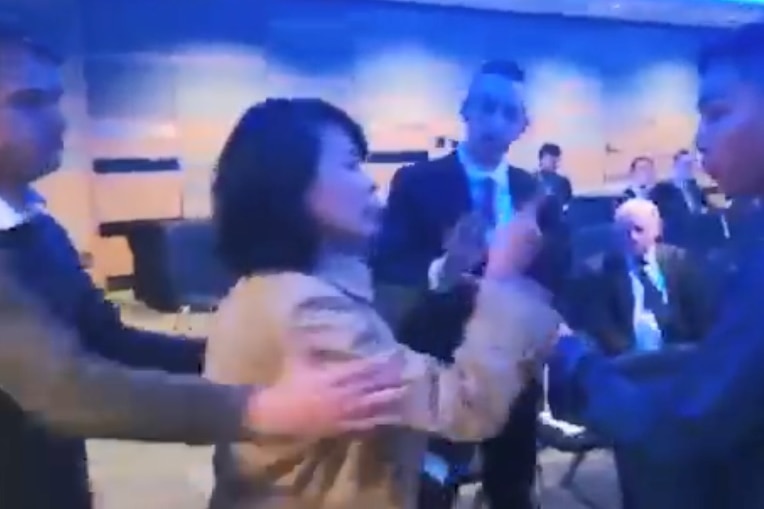 A still taken from a video showing a woman pointing at a man's face while another man tries to hold her back.