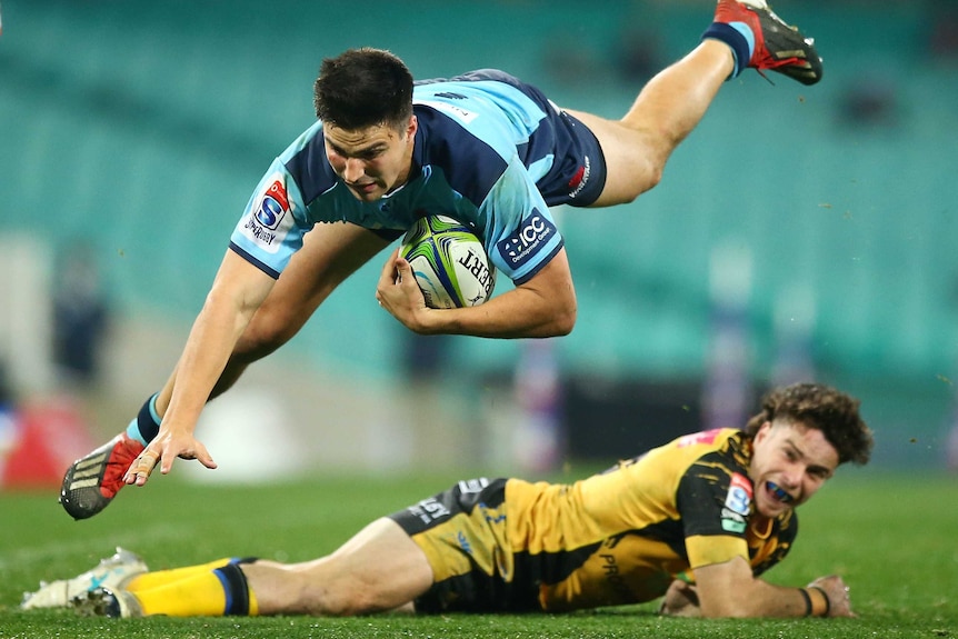 Jack Maddocks flies through the air while carrying the ball, as a Force player lays on the ground under him and watches