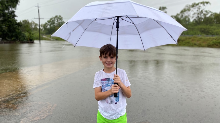 A boy stands with a big umbrella on a flooded road