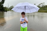 A boy stands with a big umbrella on a flooded road