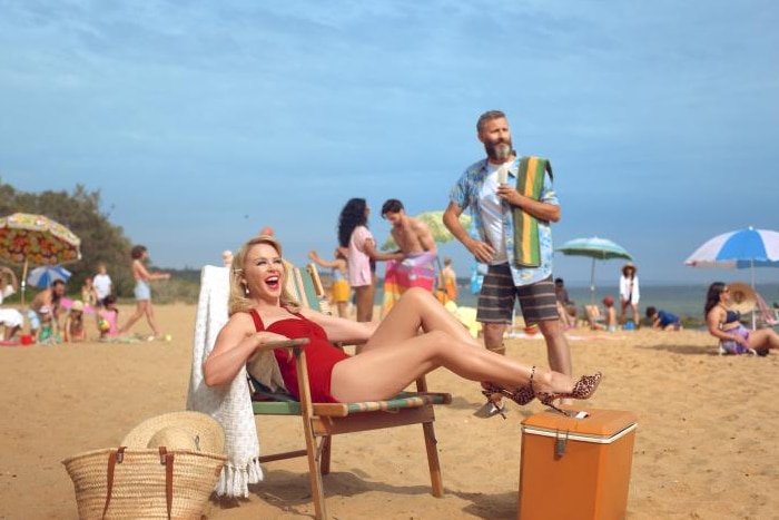 Kylie Minogue sits on a chair in a red swimsuit on Sandringham Beach.