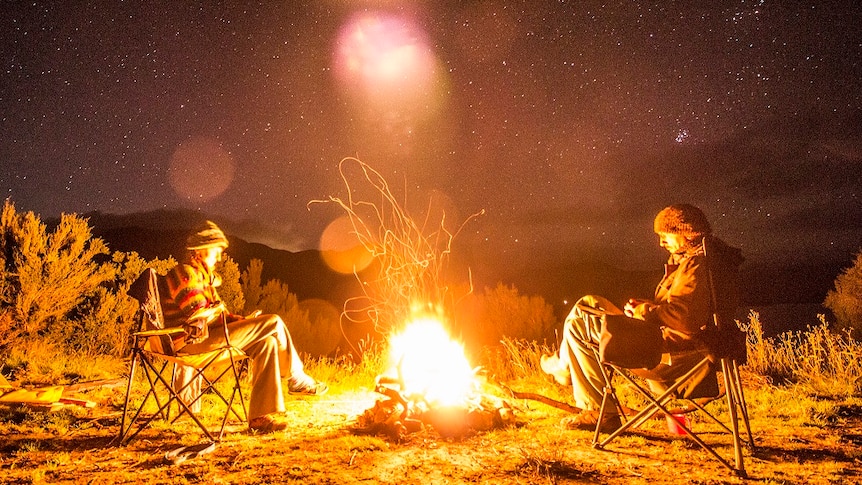 Two people sit at a campfire at night