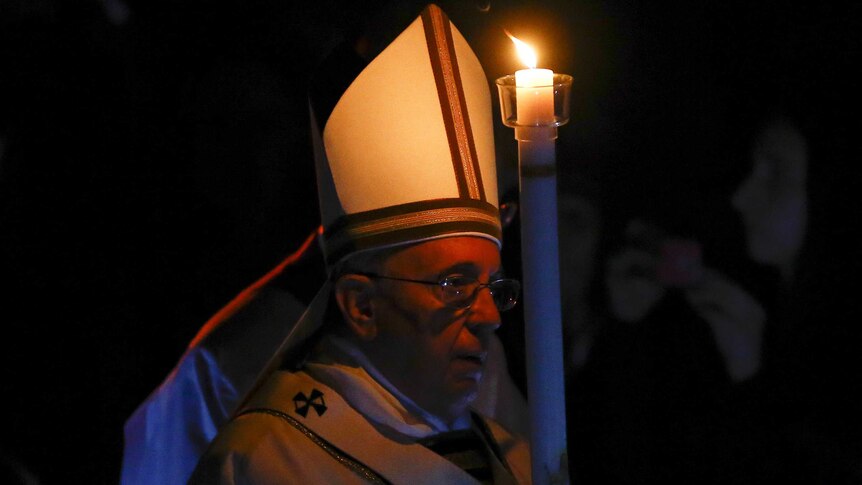 Pope Francis holds a candle as he arrives to lead the Easter mass