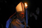 Pope Francis holds a candle as he arrives to lead the Easter mass