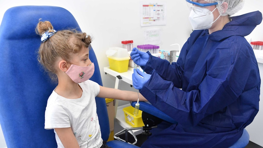 Blonde, curly-haired girl, about 8, wearing pink mask with nurse in blue smock, gloves, glasses getting medical test