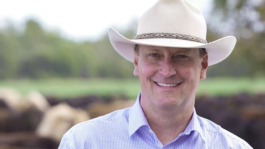 man in broad brim hat smiles in front of cattle