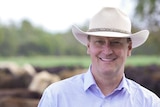 man in broad brim hat smiles in front of cattle