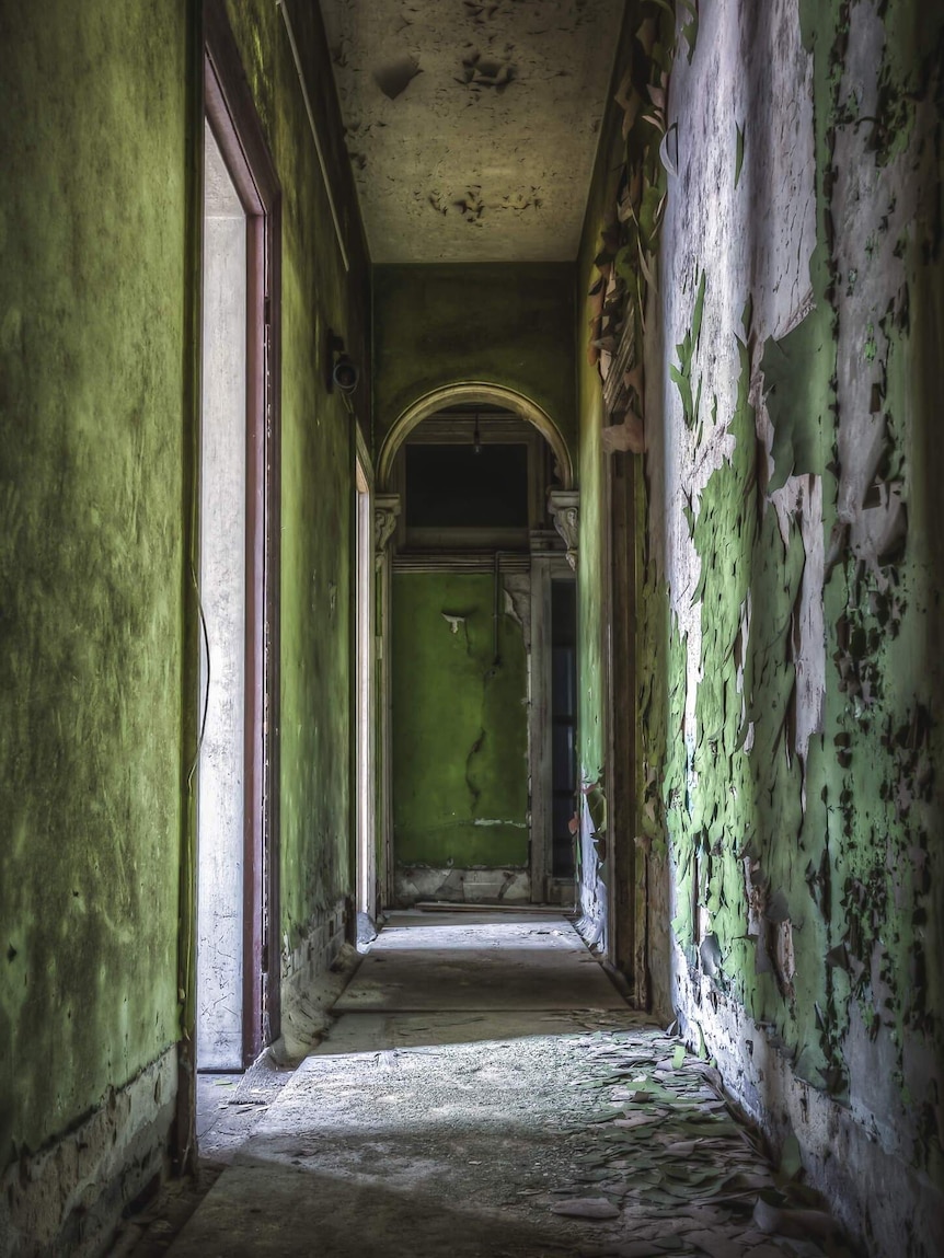 A dilapidated hallway, with peeling green wallpaper, inside the Terminus Hotel.